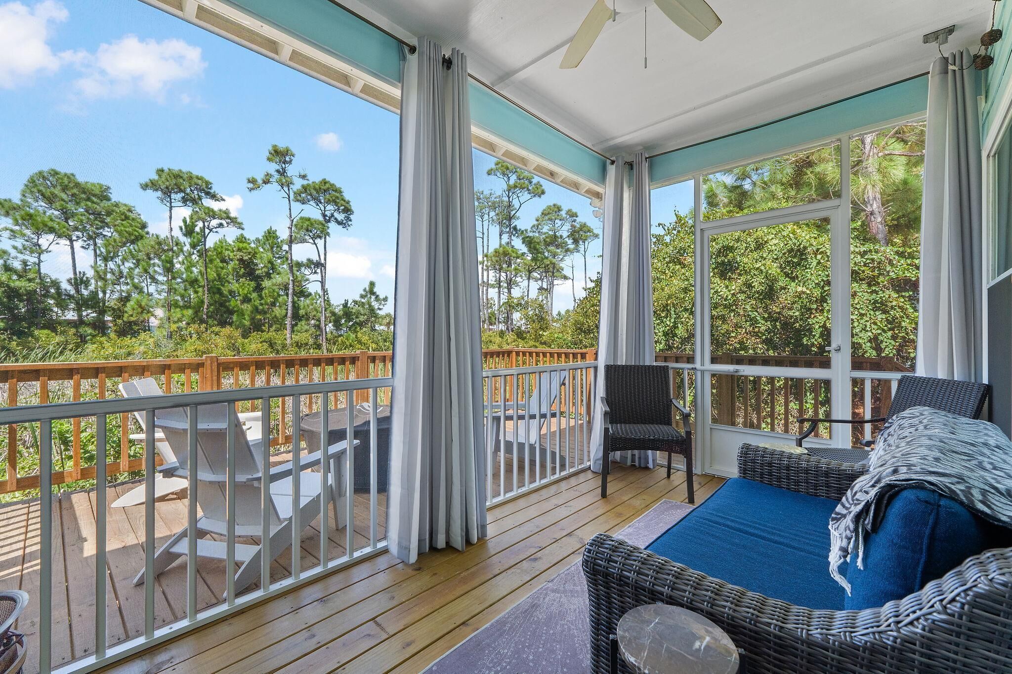 A covered outdoor deck with a view of trees, a wicker sofa, and a dining table.
