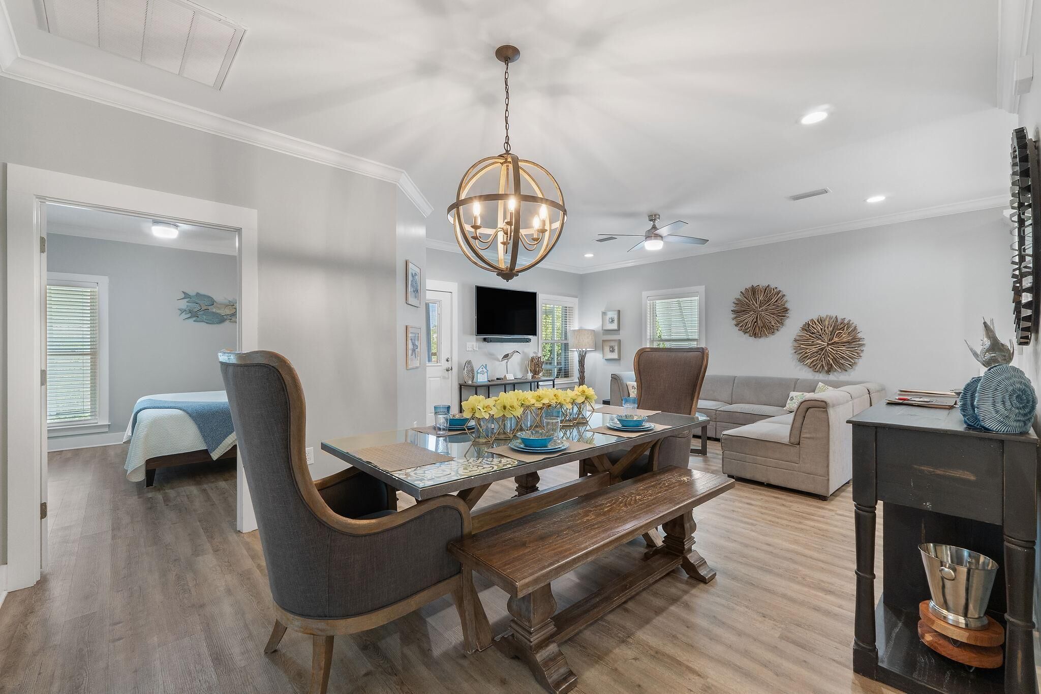 A dining area with a chandelier, a television mounted on the wall, and a sofa in the background.
