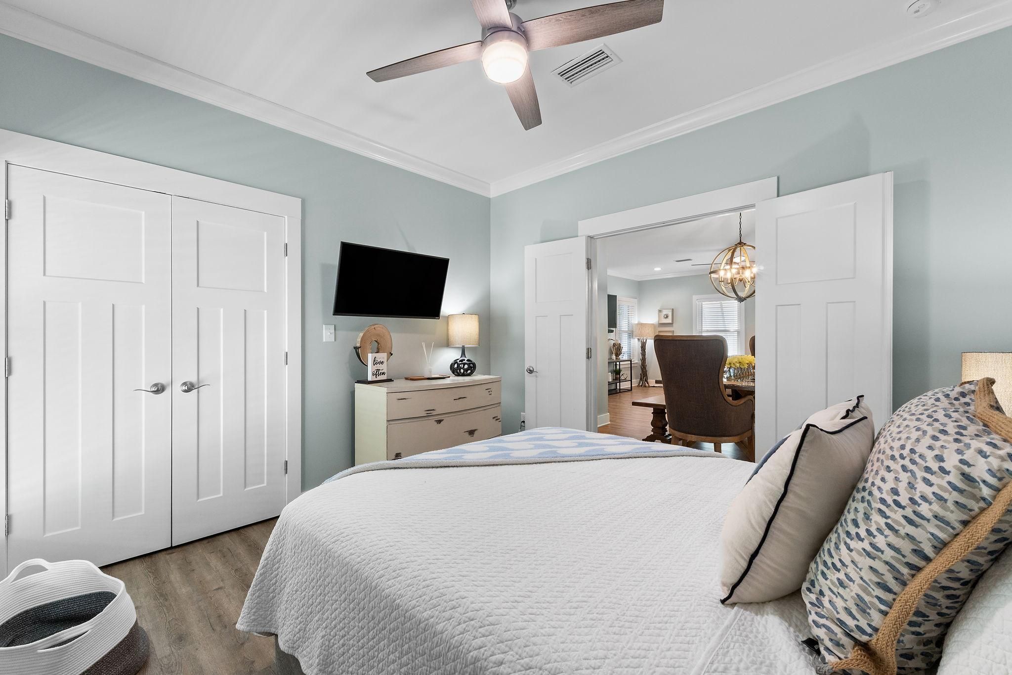 A bedroom with a bed, a dresser, a television, and a ceiling fan.