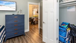 A room with a wooden floor, a blue dresser with orange handles, a bed with a striped blanket, and a door leading to a hallway.
