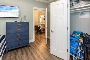 Una habitación con piso de madera, un aparador azul con pomos naranjas, una cama con manta a rayas y una puerta que da a un pasillo.
