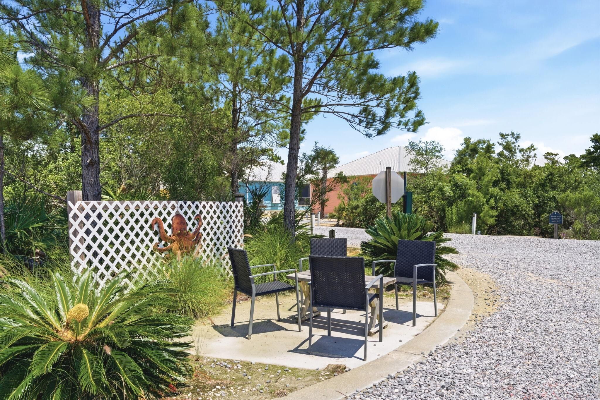 An outdoor seating area with chairs and tables, surrounded by trees and a white lattice fence.
