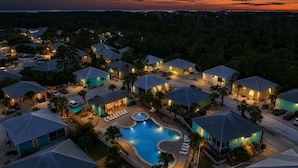 Um resort com várias casas, uma piscina e vista para o oceano ao pôr do sol.
