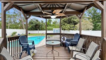 A covered outdoor deck with a pool, lounge chairs, and a table.