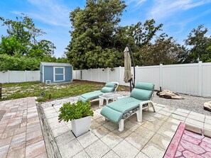 Ein Hinterhof mit Terrassenmöbeln, einem kleinen Gartenhaus und einem weißen Zaun.