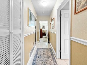 A hallway with a patterned rug, a door on the right, and a framed picture on the wall. - Azure Bungalow: Pool, Gazebo, & Beach Vibes, A/C, 15 mins from Anna Maria Island (Bradenton)