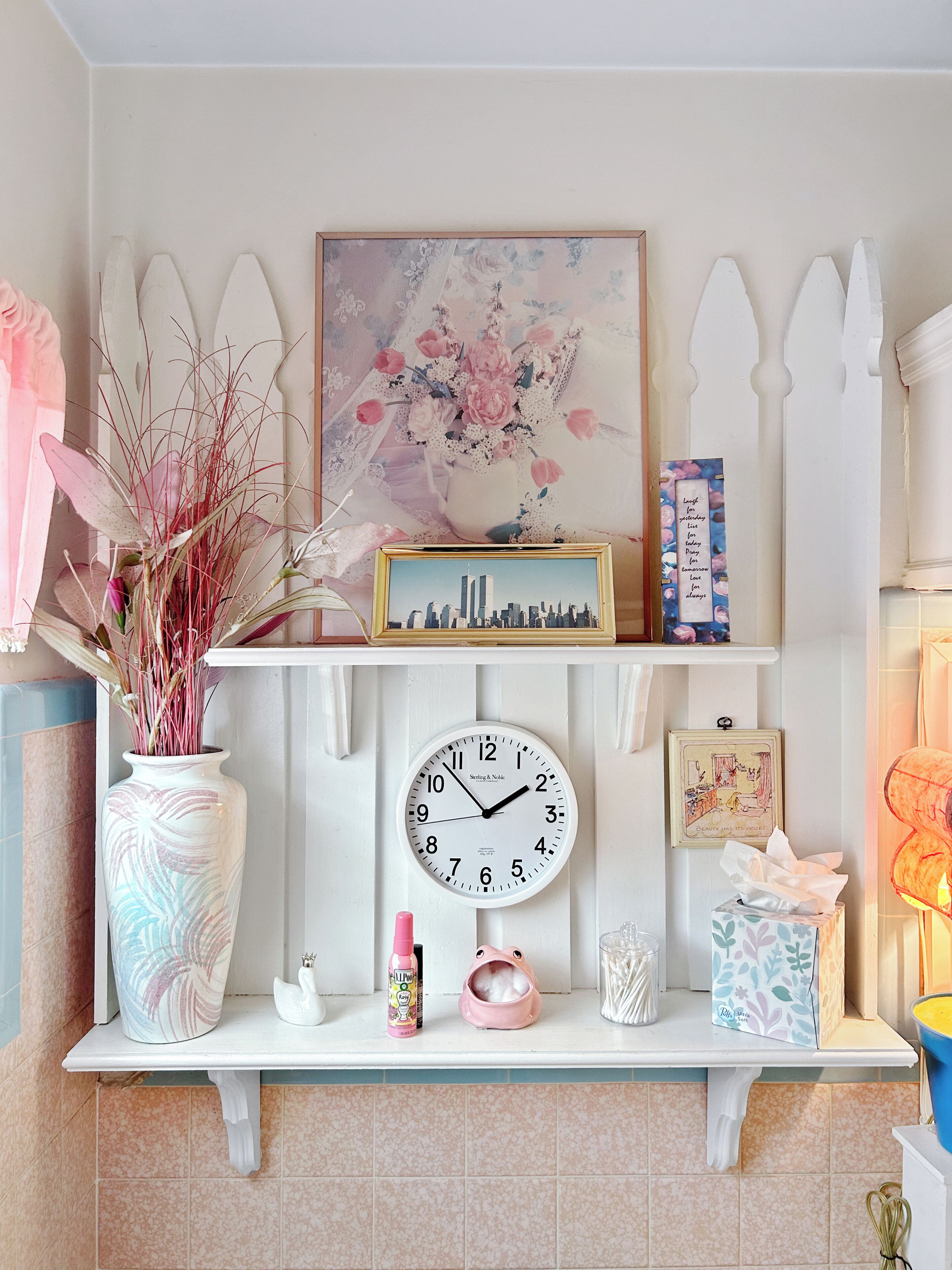 A wall-mounted clock, a framed picture, and a vase with dried plants.