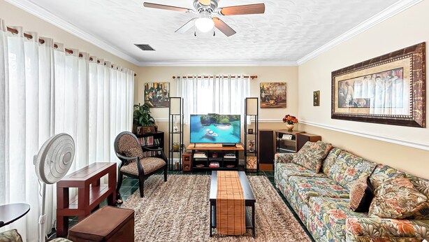 A living room with a ceiling fan, a television, a sofa, a chair, and a coffee table. - Azure Bungalow: Pool, Gazebo, & Beach Vibes, A/C, 15 mins from Anna Maria Island (Bradenton)