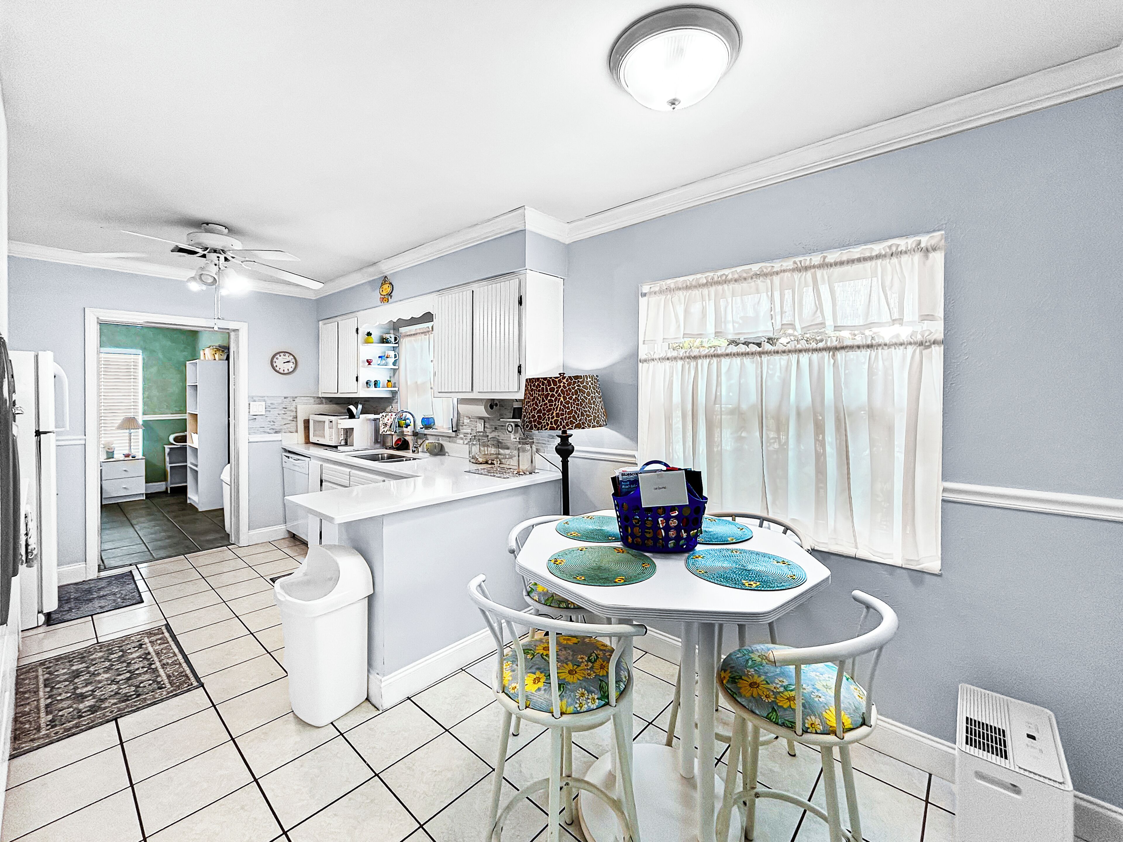 A kitchen with white cabinets, a dining table with chairs, and a window with curtains.