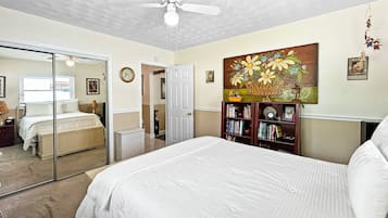A bedroom with a bed, a ceiling fan, a bookshelf, and a painting on the wall.
