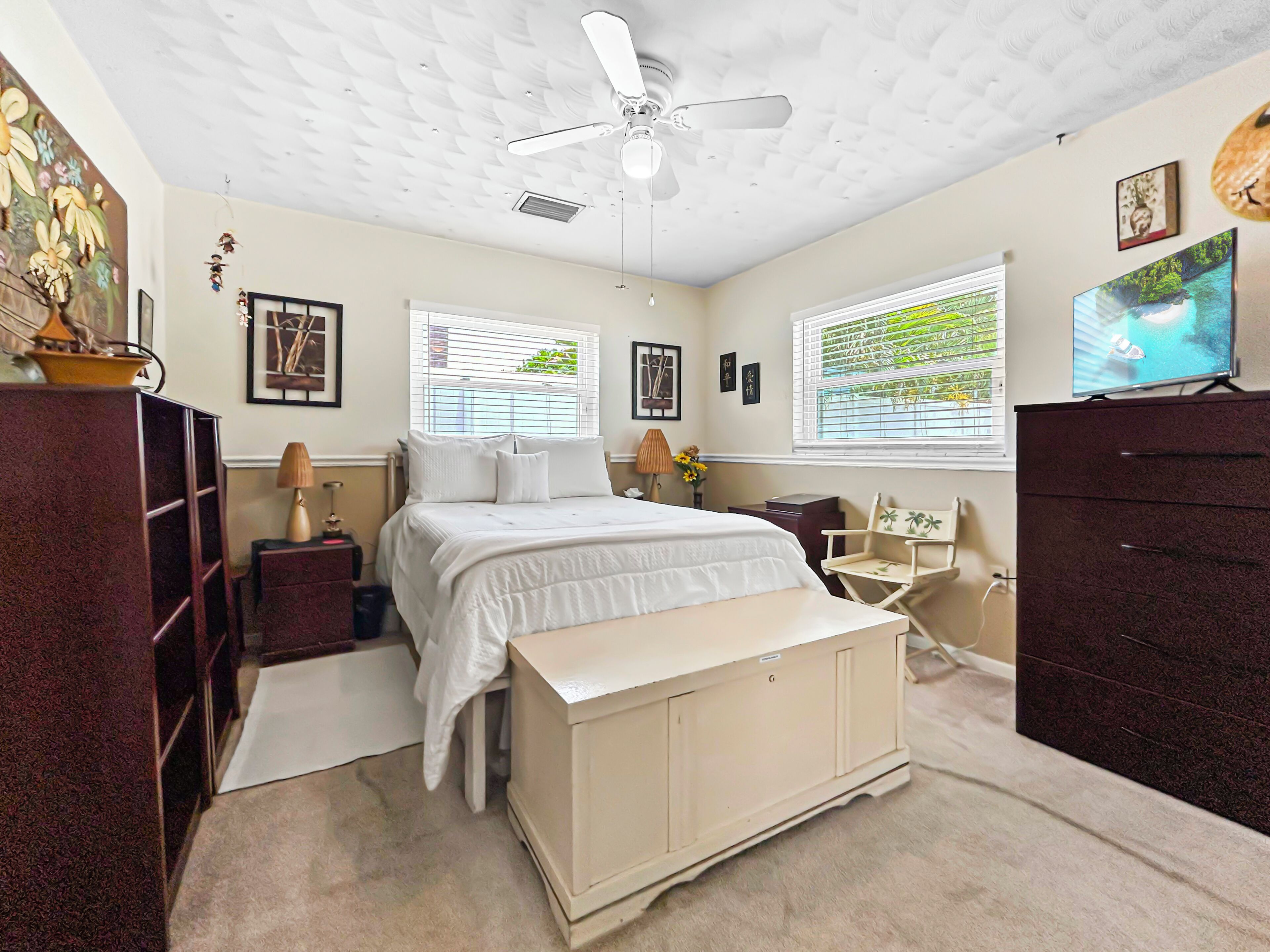 A bedroom with a bed, a desk, a chair, a wardrobe, a ceiling fan, and a television.