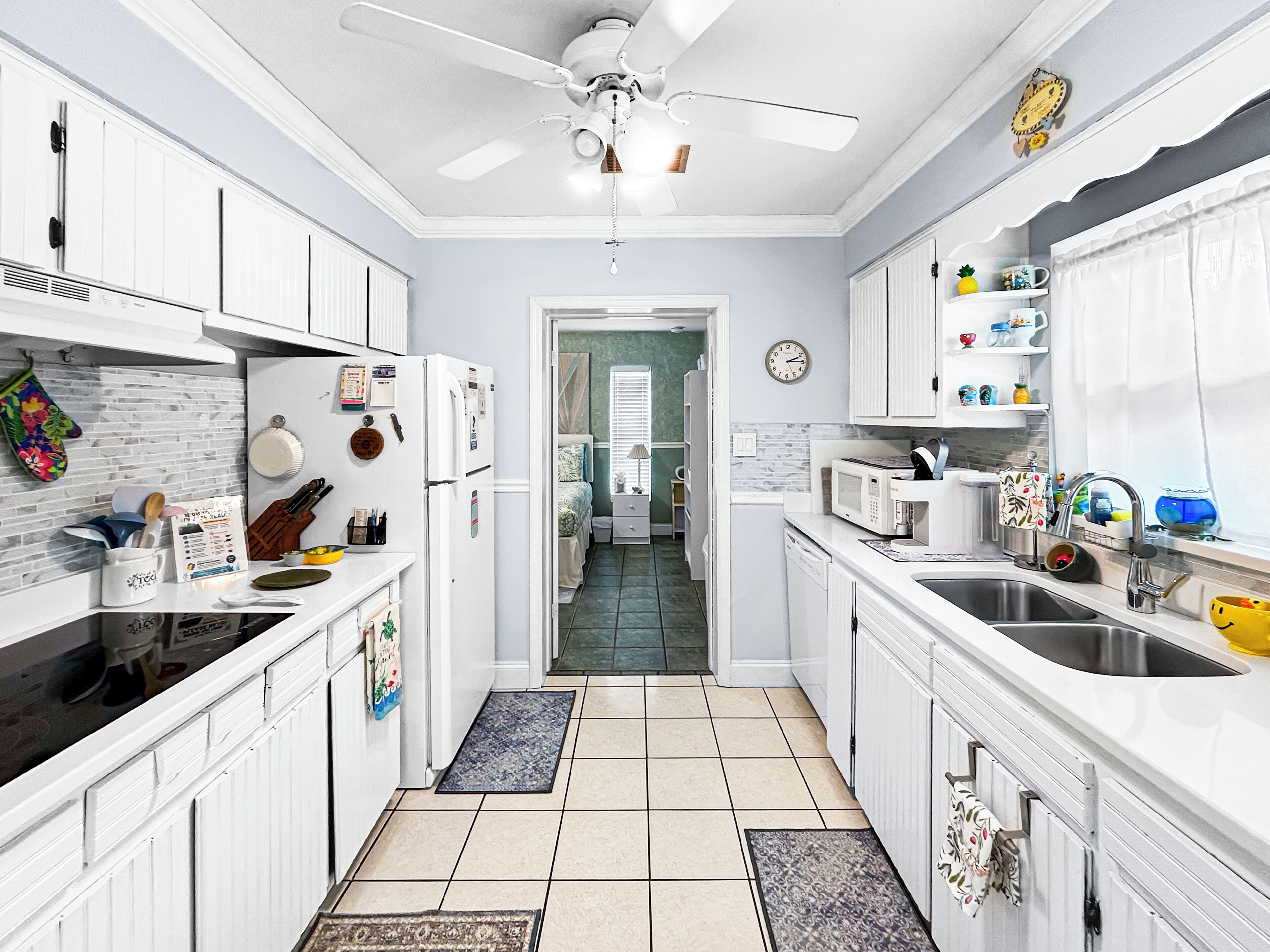 A modern kitchen with white cabinetry, a ceiling fan, a microwave, and a sink.