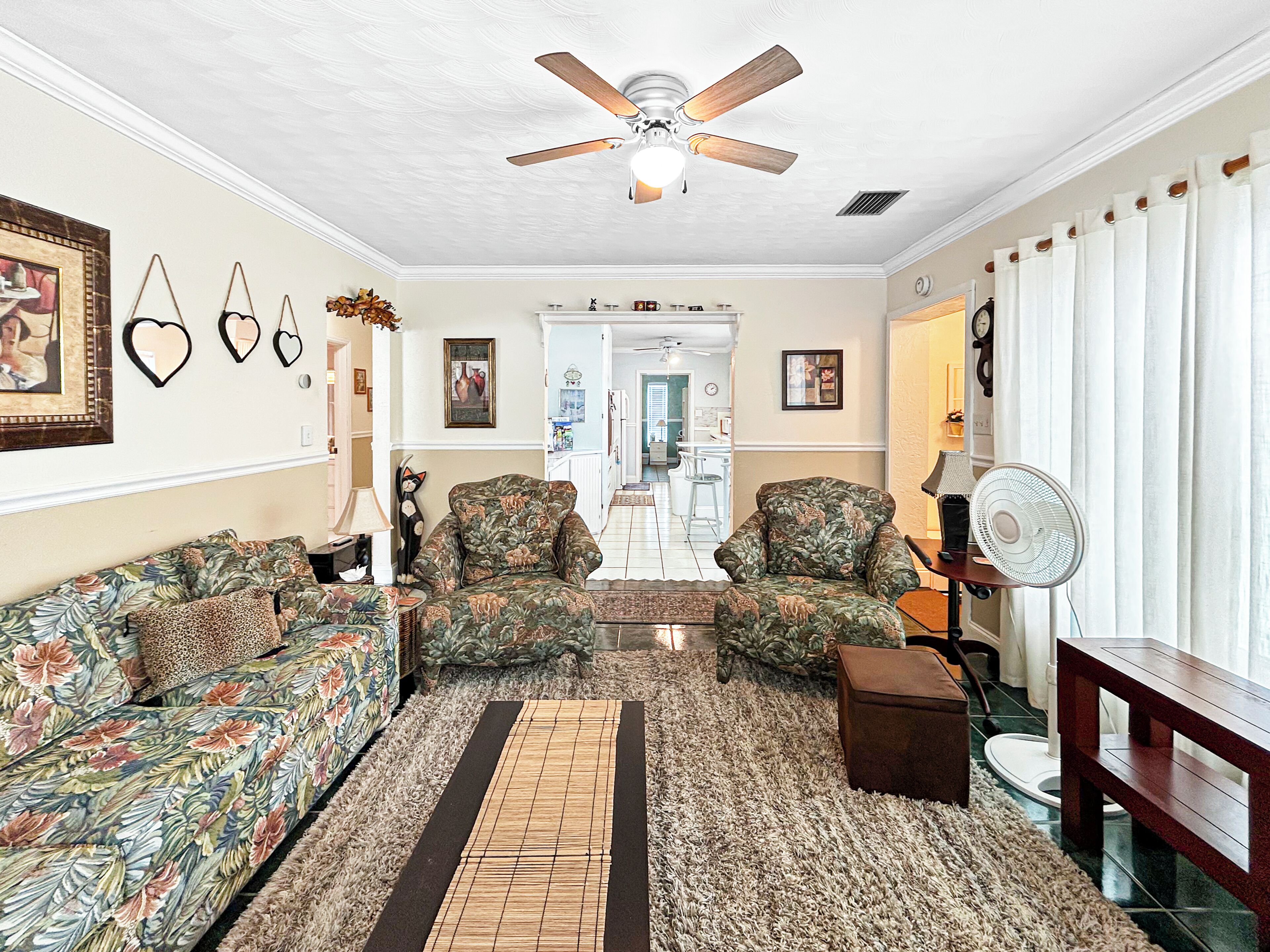 A living room with a ceiling fan, patterned sofas, a rug, and a wooden bench.