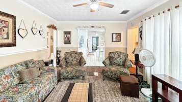 A living room with a ceiling fan, patterned sofas, a rug, and a wooden bench.