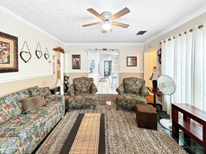 A living room with a ceiling fan, patterned sofas, a rug, and a wooden bench. - Azure Bungalow: Pool, Gazebo, & Beach Vibes, A/C, 15 mins from Anna Maria Island (Bradenton)