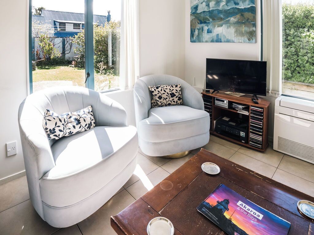 A living room with two white armchairs, a coffee table, a flat-screen TV, and a bookshelf.