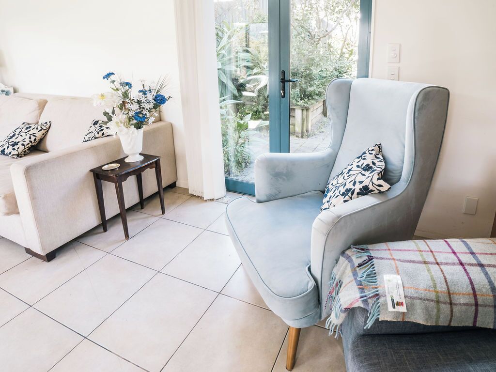 A living room with a light blue armchair, a beige sofa, and a small table with a vase of flowers.