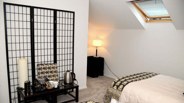 A bedroom with a bed, a nightstand with a lamp, a window with blinds, and a shoji screen. - Spacious Villa in the Heart of Akaroa (Akaroa)