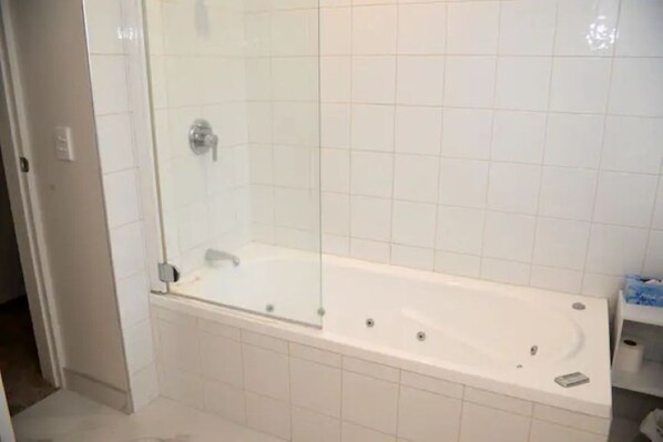 A bathroom with a glass-enclosed shower, a white bathtub, and a tiled wall.