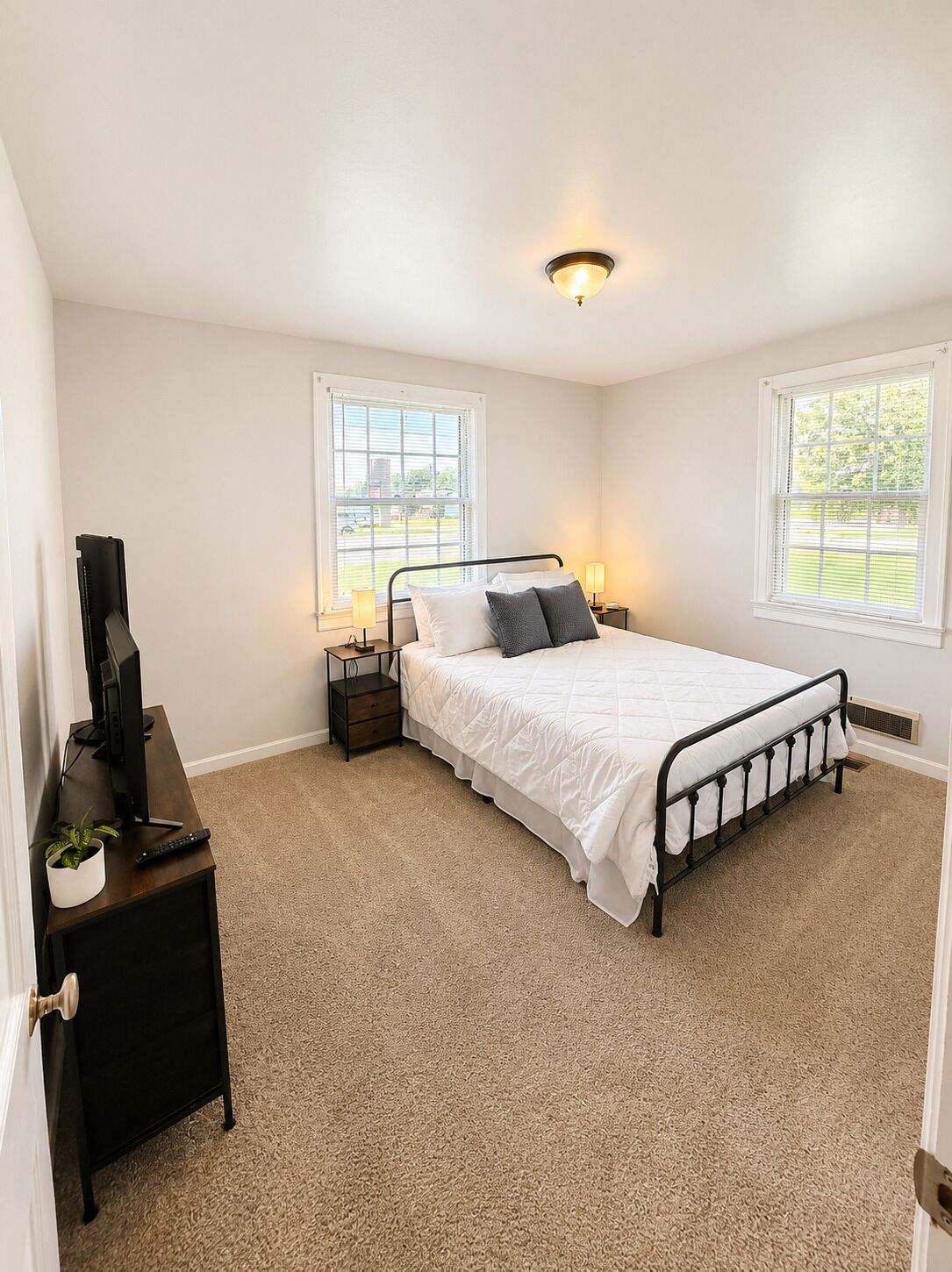 A bedroom with a bed, bedside tables, a television, and a window.