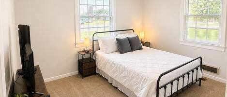 A bedroom with a bed, bedside tables, a television, and a window.