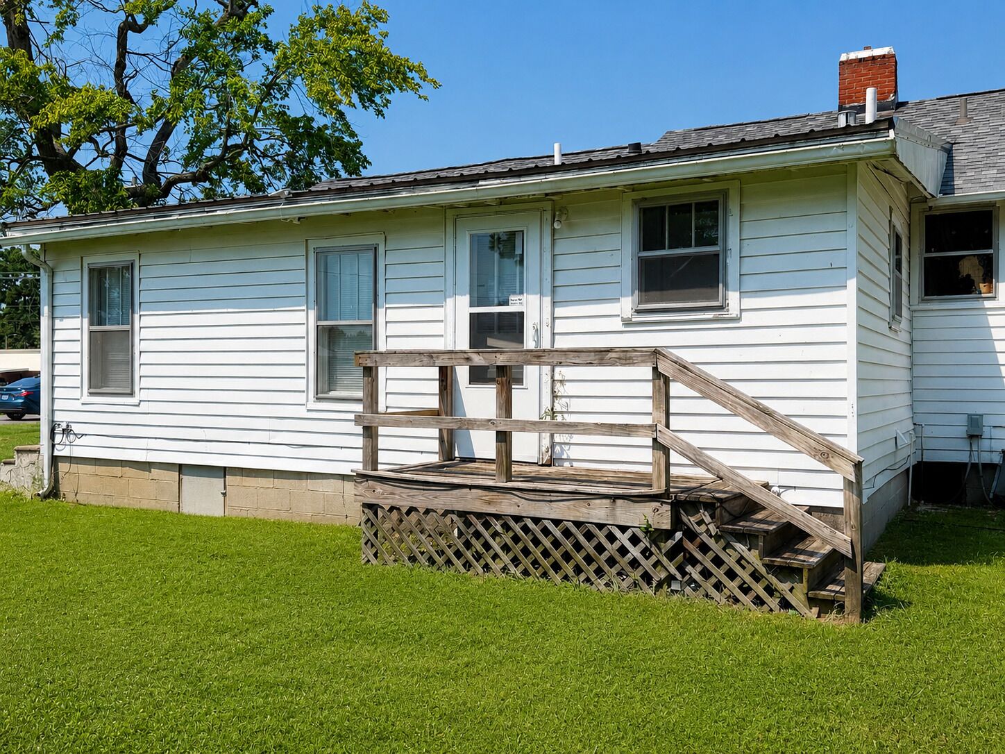 A single-story white house with a wooden porch and a brick chimney.