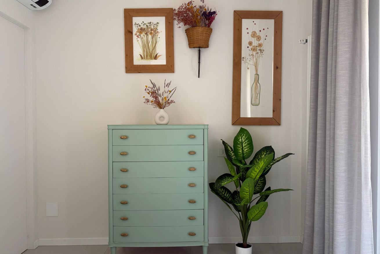 Une pièce avec une commode de couleur turquoise, une plante en pot et deux œuvres d’art encadrées accrochées au mur.
