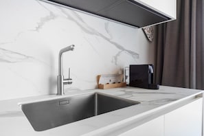 Une cuisine dotée d’un évier moderne en acier inoxydable, d’une hotte intégrée et d’une machine à café posée sur le plan de travail.