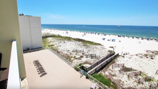 A beach view from a balcony with a wooden deck, a sandy beach area, and a clear sky. - Boardwalk 486 (Gulf Shores)