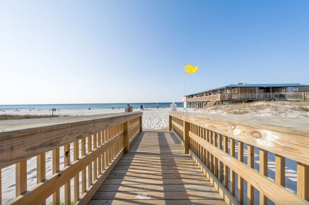 A wooden boardwalk leading to a beach with a building on the right.