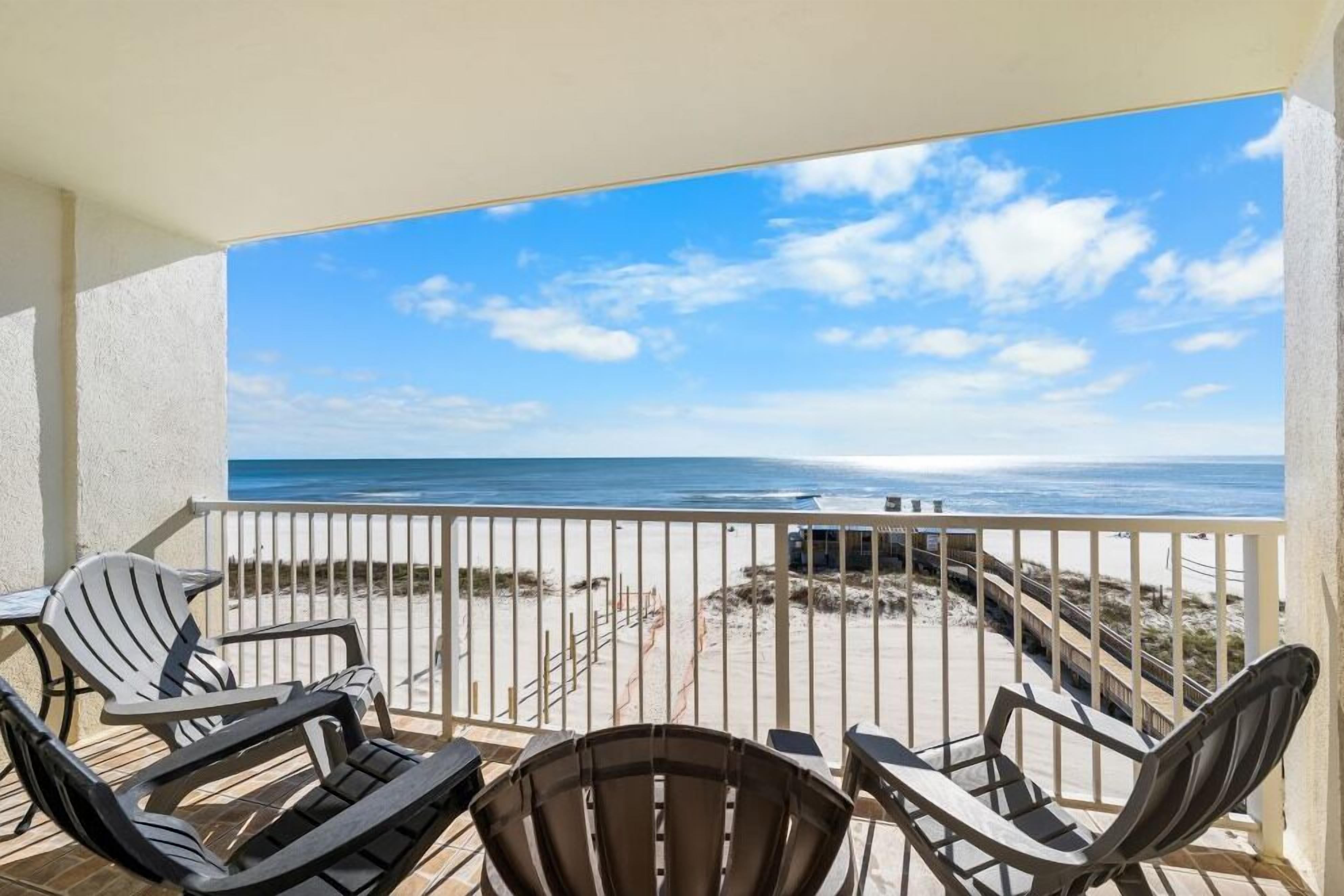 A balcony with a view of the beach and ocean, featuring several chairs and a table.