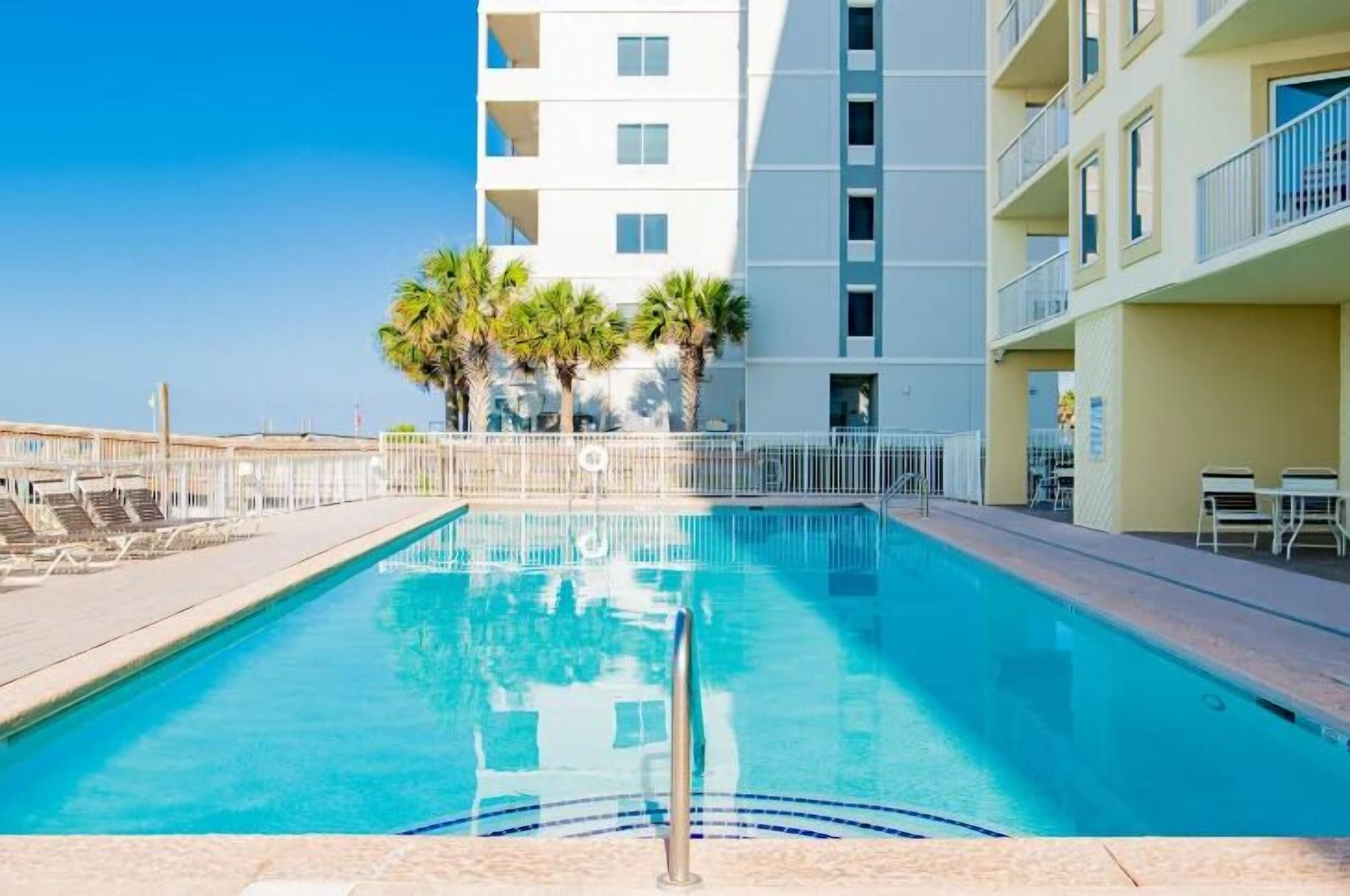 A swimming pool with a clear blue water, surrounded by a white fence and palm trees.