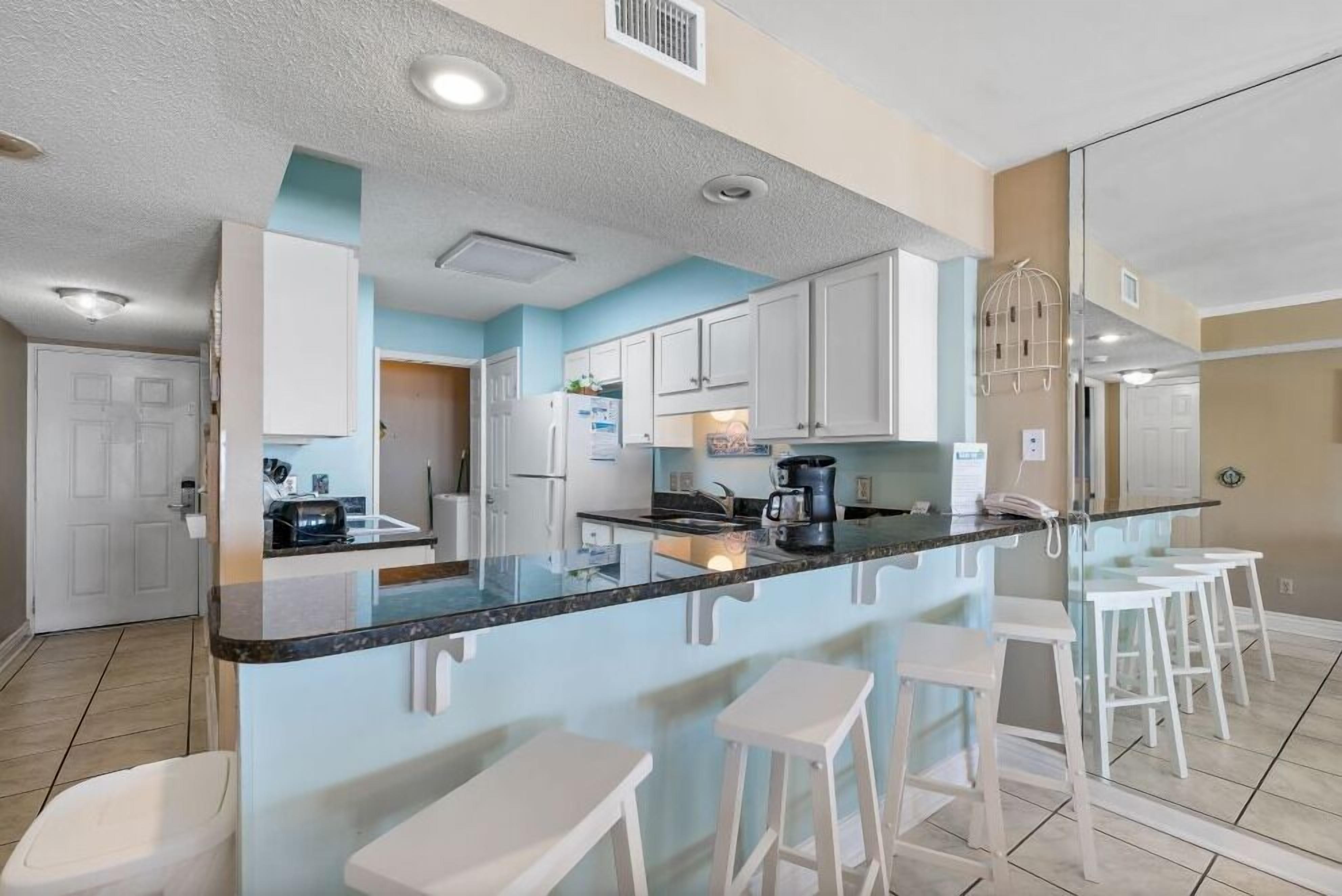 A modern kitchen with a central island, bar stools, and white cabinetry.