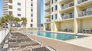 A swimming pool with lounge chairs and a building with balconies in the background. - Boardwalk 486 (Gulf Shores)