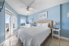 A bedroom with a bed, a ceiling fan, a window with a view, and a nightstand with a lamp. - Boardwalk 486 (Gulf Shores)