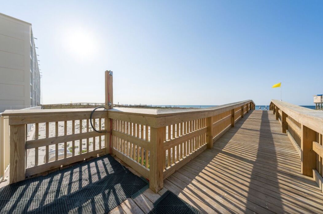 A wooden deck leading to a beach with a clear sky.