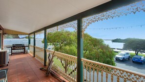 Un balcon abrité avec un barbecue, des sièges d’extérieur et une vue sur une étendue d’eau et des voitures garées.