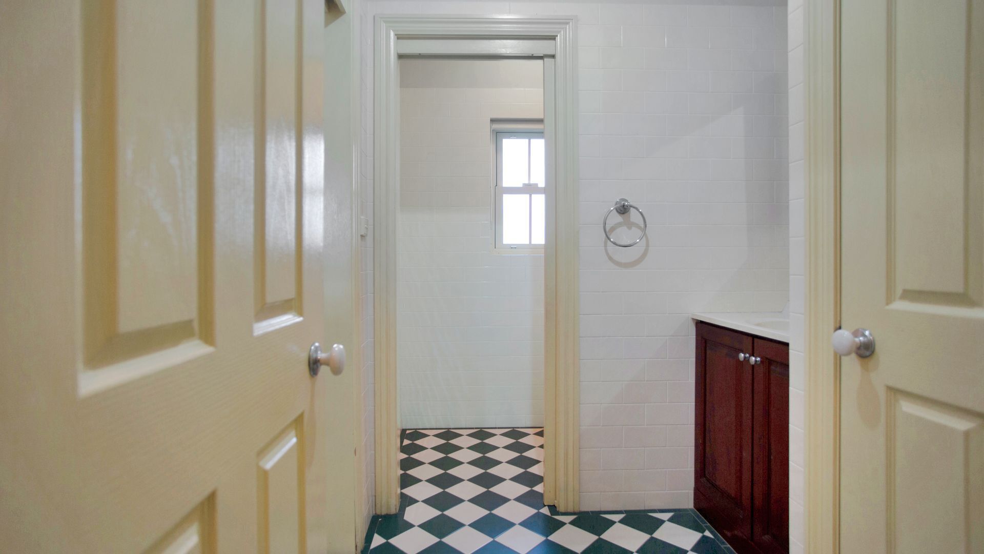A narrow hallway with a checkered floor, white walls, and a wooden cabinet.