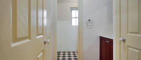 A narrow hallway with a checkered floor, white walls, and a wooden cabinet.