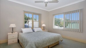 A bedroom with a bed, two bedside tables, a ceiling fan, and windows with blinds. - Rivers Edge Apartment (Tea Gardens)