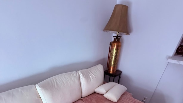 Una cama con un edredón rosa, una almohada blanca y una almohada color beige. Hay una lámpara sobre una mesita de noche.