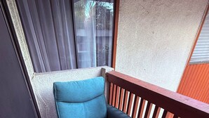 Un sofá compacto y plegable con cojín azul, colocado en un balcón con barandilla de madera y un tapete de suelo estampado.
