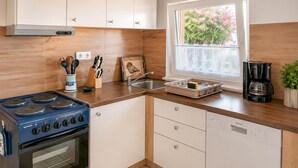 Een moderne keuken met een blauwe kookplaat, witte kasten en een raam met uitzicht op groen.