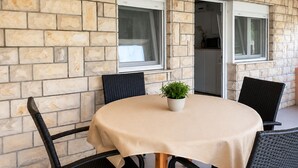 Een ronde tafel met een beige tafelkleed, omringd door vier zwarte stoelen, geplaatst tegen een stenen muur met twee ramen.