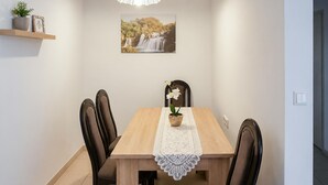 Een eetruimte met een houten tafel, vier stoelen, een plant in pot, een lijst met afbeelding en een hanglamp.