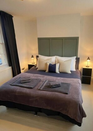 A neatly made bed with a headboard, two bedside tables with lamps, and a window with curtains. - Spacious Townhouse central Leamington with parking (Royal Leamington Spa)
