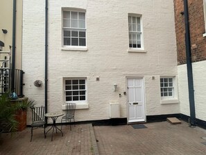 A white brick building with a door, two windows, and a small patio with a table and chairs. - Spacious Townhouse central Leamington with parking (Royal Leamington Spa)
