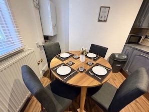 A round dining table with six chairs, a white pitcher, and a vase with flowers. - Spacious Townhouse central Leamington with parking (Royal Leamington Spa)