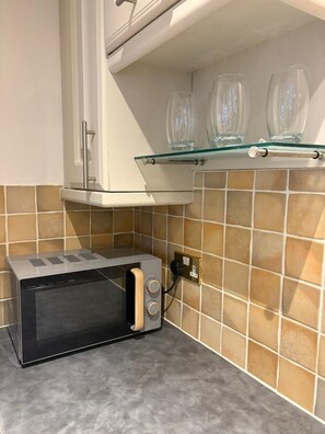 A kitchen with a microwave, a glass shelf with three wine glasses, and a tiled backsplash. - Spacious Townhouse central Leamington with parking (Royal Leamington Spa)