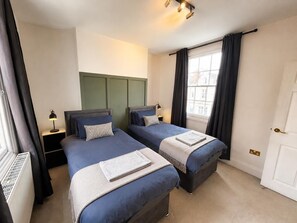 A hotel room with two beds, a radiator, a window with curtains, and a door. - Spacious Townhouse central Leamington with parking (Royal Leamington Spa)